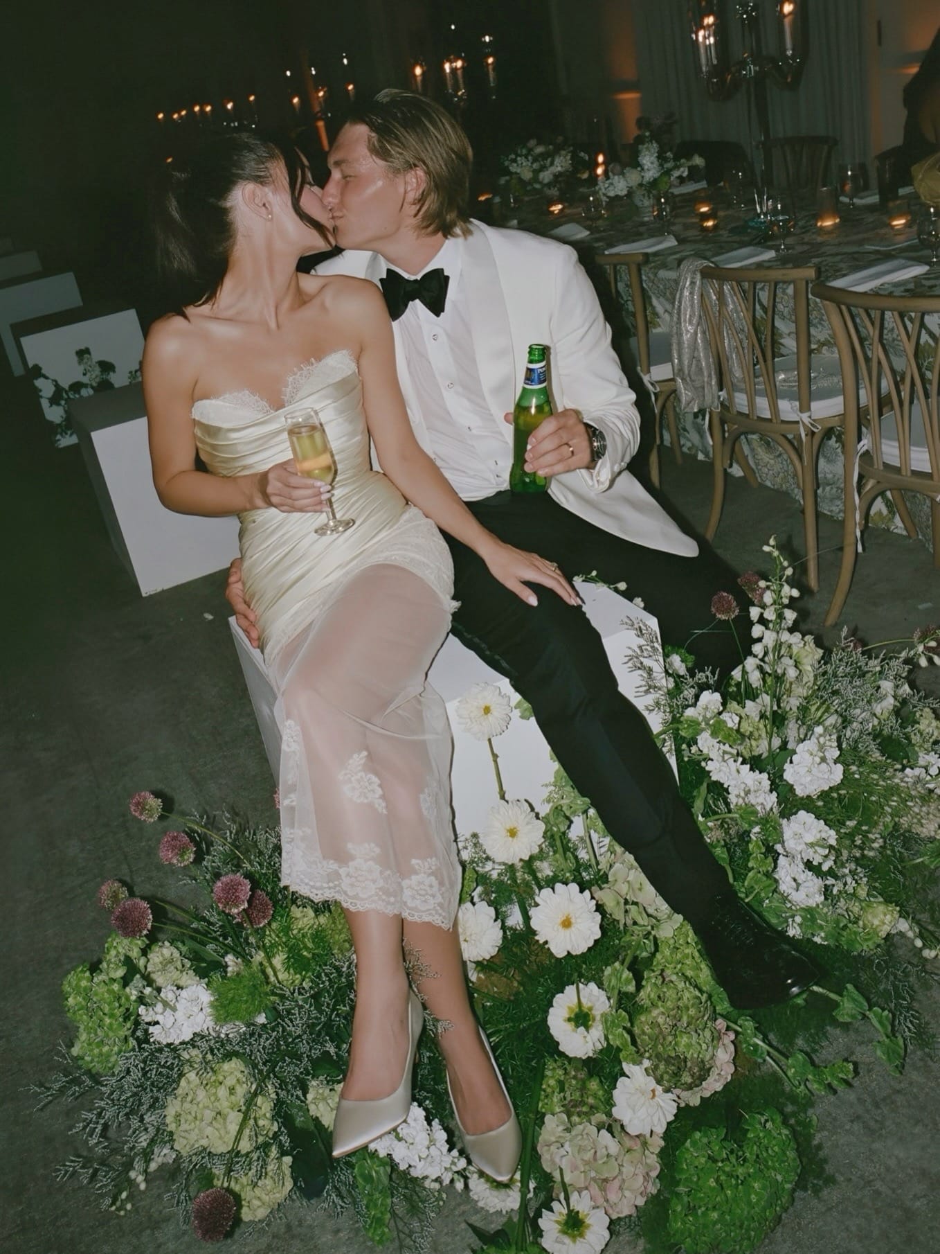 Bride in custom champagne strapless corset wedding dress with lace overlay, seated among florals at wedding reception — Jinza Bridal Los Angeles